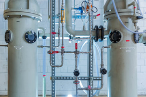 Two light gray containers connected with different pipes made of metal stand next to each other in the laboratory.